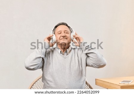 Senior man with closed eyes in living room wearing headphones listens favourite track, having nostalgic mood, enjoys songs of his youth, older generation using modern technology concept, copy space