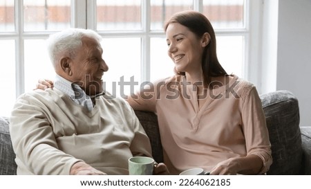 Happy mature man with grownup daughter having fun at home, chatting, talking, sharing news, sitting on cozy couch, smiling older father and young woman drinking tea coffee, enjoying leisure time Royalty-Free Stock Photo #2264062185