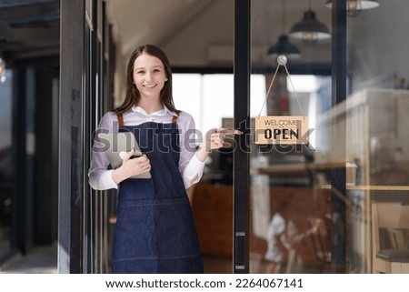 Portrait of a happy waitress standing at restaurant entrance. Happy woman owner showing open sign in her small business shop.