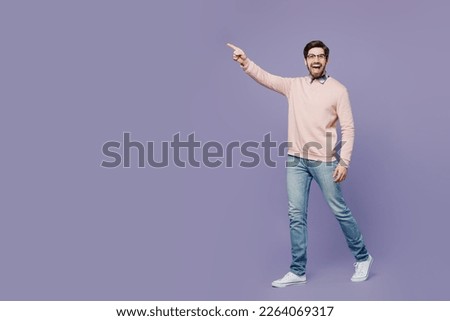 Full body sideways happy fun young IT man he wears casual clothes pink sweater glasses walking going strolling point index finger aside on area isolated on plain pastel light purple background studio