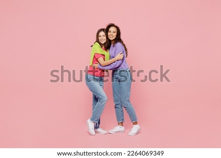 Full body young two friends smiling happy fun cool cheerful positive women 20s wear green purple shirts together stand look camera hug homie isolated on pastel plain light pink color background studio