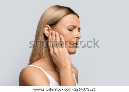 Tinnitus. Profile of sick female middle aged blonde woman having strong ear pain, touching her painful head, isolated on grey studio background, panorama with copy space Royalty-Free Stock Photo #2264073521