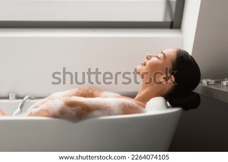 Relaxed Female Taking Bath With Foam Lying In Bathtub In Modern Bathroom Indoors. Woman Bathing Enjoying Bodycare Routine With Eyes Closed At Home. Spa And Wellness. Side View, Selective Focus Royalty-Free Stock Photo #2264074105