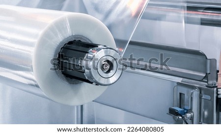 Automatic polyethylene plastic bag production machine with lighting effect. Close-up of the roller of the plastic bag production machine in the light blue scene. product packaging concept Royalty-Free Stock Photo #2264080805