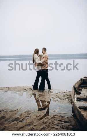 man and woman hugging on the lake shore, cold foggy weather. romantic photo in beige clothes. to hug a woman, a love story. beige sweaters. romantic photos against the background of a foggy lake