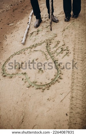 draw a heart on white sand. romantic picture of a beloved girl on the sand. hold hands