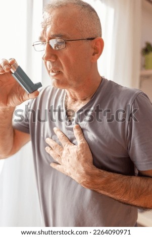 An asthmatic mature man  who takes an inhaler and has an asthma attack. He has a problem with asthma and holding an inhaler. Royalty-Free Stock Photo #2264090971
