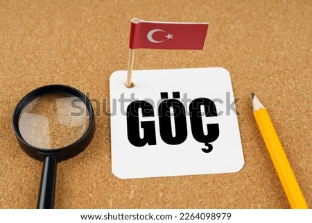 On the table is the flag of Turkey, a pencil, a magnifying glass and a sheet of paper with an inscription in Turkish translated into English - Emigration.
