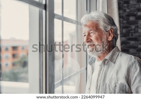 Happy thoughtful older 70s man looking out of window away with hope, thinking of good health, retirement, insurance benefits, dreaming of future. Elderly pensioner waiting meeting with family