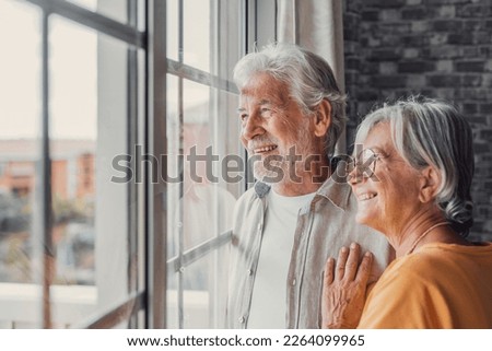 Happy bonding loving middle aged senior retired couple standing near window, looking in distance, recollecting good memories or planning common future, enjoying peaceful moment together at home. Royalty-Free Stock Photo #2264099965