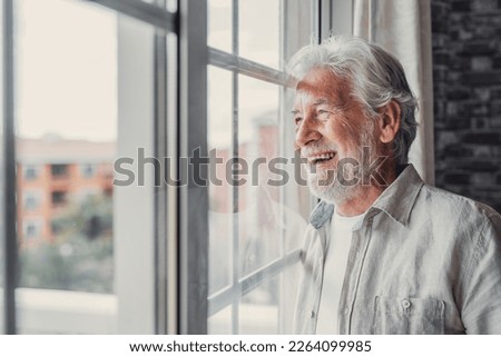 Happy thoughtful older 70s man looking out of window away with hope, thinking of good health, retirement, insurance benefits, dreaming of future. Elderly pensioner waiting meeting with family