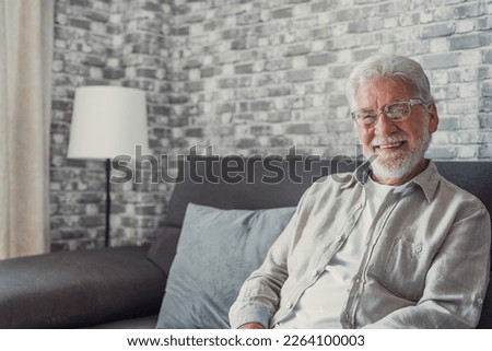 Portrait of happy mature 80s man sit on couch at home look at camera posing relaxing on weekend, smiling positive senior 70s grandfather rest on sofa at home or retirement house, show optimism