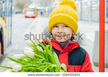 Beautiful boy on city street near bus stop with bouquet of tulips in his hands..