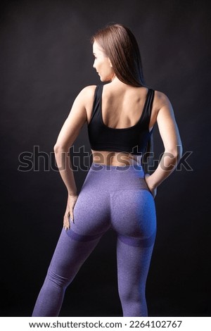 A young healthy girl in a sports top and leggings poses in the studio against a black background.