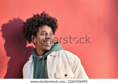 Authentic photo of young happy African American cool hipster teen guy face laughing on red city wall lit with sunlight. Smiling cool rebel gen z teenager model looking away at advertising copy space.