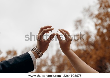 Male and female hands as silhouettes hold wedding rings facing each other. The bride and groom put their wedding rings against the sky. Weddings and gold wedding rings. Royalty-Free Stock Photo #2264108675