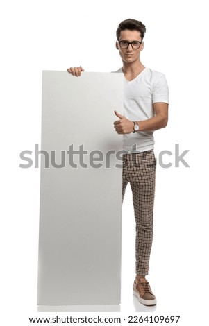 casual young man showing white billboard and making thumbs up on white background 