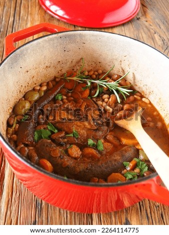 French Cassoulet in a red cast iron cooking pot on a wooden rustic table, vertical picture