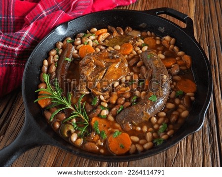 French Cassoulet  in a cast iron skillet, on a wooden table with a red dish towel