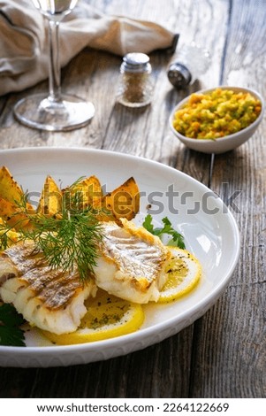 Fish dish - fried cod with baked potatoes and fresh vegetables on wooden table 