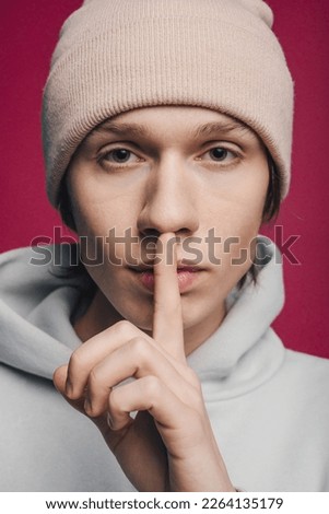 Handsome young man wearing hat holding his finger near his lips asks for silence,isolated over pink background. Silence and secret concept.