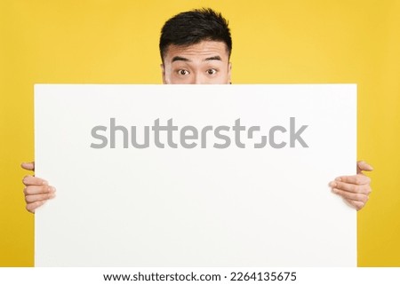 Surprised chinese man hiding behind a blank panel