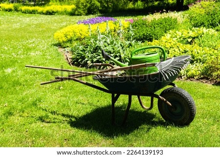 A gardeners wheelbarrow with the gardening tools in the gardens. Gardening concept Royalty-Free Stock Photo #2264139193