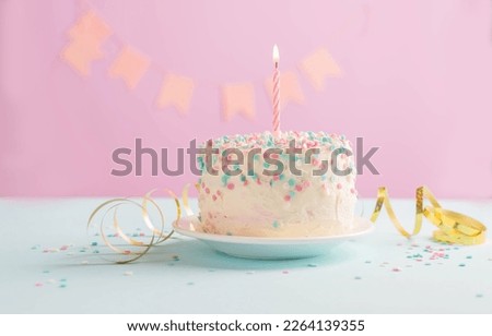 Festive cake with one candle on the background of festive pink wall with gifts flags in serpentine Royalty-Free Stock Photo #2264139355