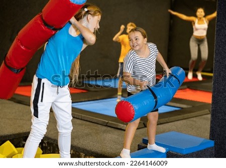 Children girls having fun and playing with inflatable sticks on the trampoline arena while spending time together on weekend