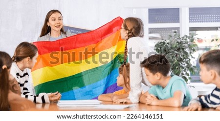 Young female teacher showing flag of LGBT to schoolchildren preteens and explaining LGBTQ social movements in classroom Royalty-Free Stock Photo #2264146151