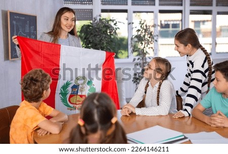 Students sitting in class and listening carefully to female teacher holding Peru flag in hands