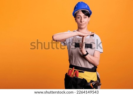 Exhausted industrial engineer doing timeout sign over yellow background, showing t shape symbol with hands. Woman builder refusing to work and asking for break or pause, studio shot.