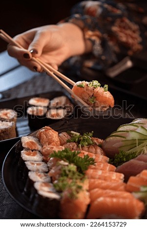 Eating sushi with chopsticks. Japanese food sushi roll in restaurant. California sushi roll set with salmon, vegetables, flying fish roe and caviar closeup. Japan restaurant menu Royalty-Free Stock Photo #2264153729