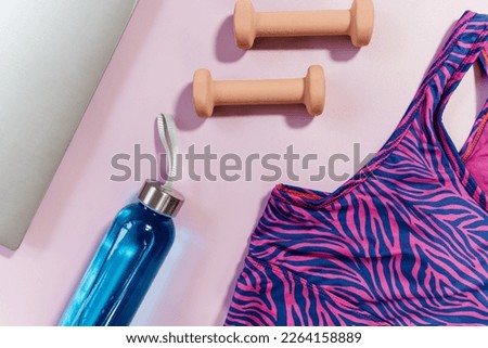 Set of accessories for fitness, yoga. Bra, pink block for yoga, bottle for water, dumbbells, sneakers, skipping rope, laptop on pink pastel background. Sports gear, minimalistic background. Close up