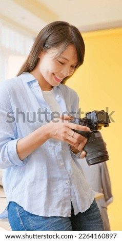 asian female photographer sitting on table is using digital camera to check up pictures in studio and she satisfied with the work
