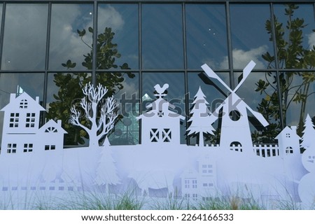 White paper cut out in the shape of a village on winter in front of the glass window.