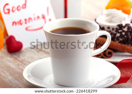 love design - morning coffee in white cup, little red heart, note  and beautiful cup-cake on wooden surface 