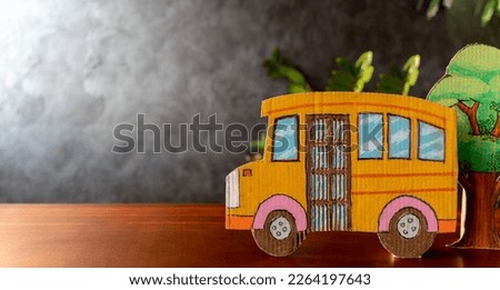 Yellow school bus made of cardboard and plants arranged on students' desks. Blackboard background, back to school concept. There is empty space that can put picture text.
