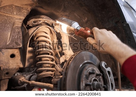 A car mechanic inspects springs, shock absorbers and suspension with a flashlight. Car on a repair stand. Technical service station for car. Royalty-Free Stock Photo #2264200841