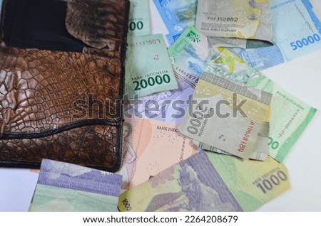 leather wallet on top of rupiah bills arranged in such a way on a white background