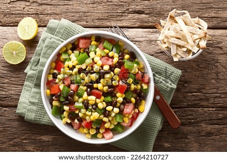 Mexican style colorful fresh vegetable salad made of beans, corn, tomato and bell pepper served in bowl, baked tortilla strips, photographed overhead on wood (Selective Focus, Focus on the salad) Royalty-Free Stock Photo #2264210727