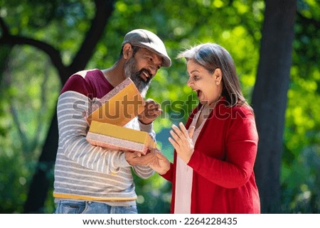 Indian man giving surprise gift to woman at park.