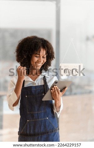 Attractive African American barista woman in apron feeling happy while working at coffee and bakery shop.