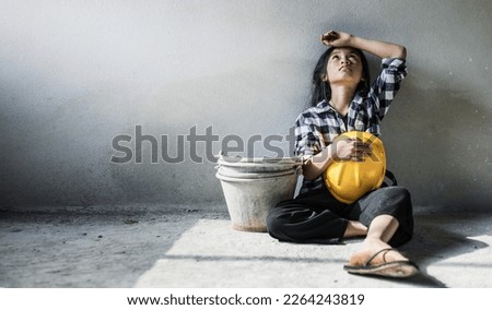 Exhausted little girl sitting on floor concrete wall background. child labor and exploitation Royalty-Free Stock Photo #2264243819