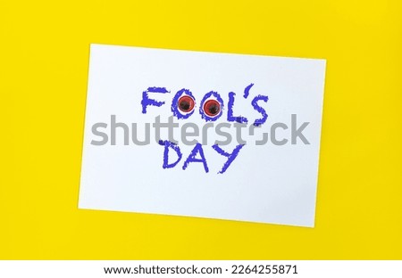 Text word Fool's day on sheet of paper with funny eyes and. 1 april message handwritting on sheet of paper. Bright yellow background. International humor day.