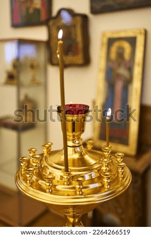 a large and tall Orthodox candle burns in a church candlestick. in the background out of focus icons