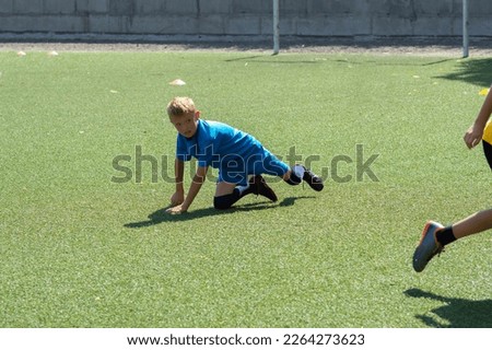 children's football, a boy of European race is studying on a green field with a ball in a blue uniform