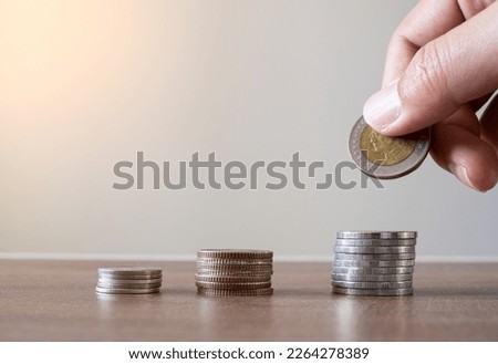 A close-up photo of a pile of coins on a wooden table. A person's hand is picking up coins.