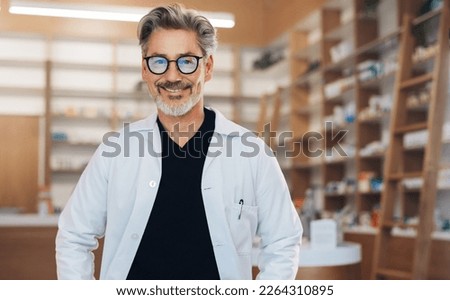 Portrait of a male pharmacist standing in a drug store in a white lab coat. Senior man working in a pharmacy. Mature healthcare worker smiling at the camera. Royalty-Free Stock Photo #2264310895
