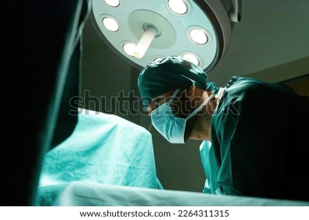 motivated caucasian surgeon trying help patient under drapes. male nurse wear mask determined performing surgery in hospital. professional surgical staff working hard save patient in operating room.